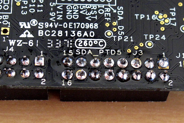 Pin 1 (the rightmost pin in the top row) shows another soldering flaw—there is enough solder, but it hasn't flowed onto the pad completely.  Such "cold-solder" joints can be fixed by reheating the pin and pad, without adding more solder. Some of the other pins in this picture also show cold-solder joints, though less severely.  Whenever bare copper appears on the pad, the joint needs to be reheated.  (See pin 14 to the right of pin 16, for example.)